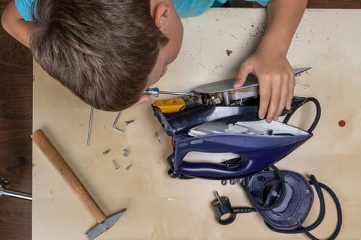 boy helps his mother. a funny master repairs an electric iron on the table using tools. Disassembled electric iron.