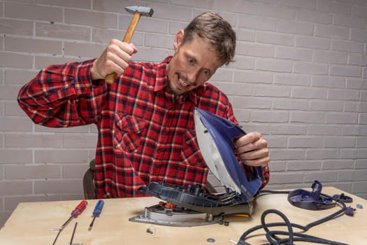 a funny and annoyed grief-stricken master repairs an electric iron. the master repairs the iron in the workshop on the table using tools. Disassembled electric iron.