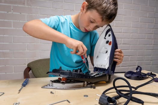 boy helps his mother. a funny master repairs an electric iron on the table using tools. Disassembled electric iron.