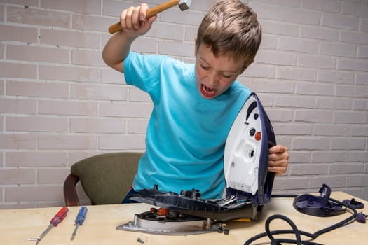 boy repairs an electric iron. a funny master repairs an electric iron on the table using tools. Disassembled electric iron.