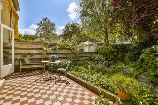 an outside area with a table and chairs in the middle, surrounded by trees and plants on both sides there is a checkered