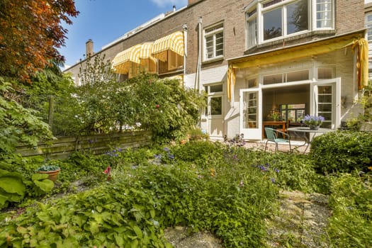 an outside area with flowers and plants in the fore - windowed yard, next to a brick wall that has been painted yellow