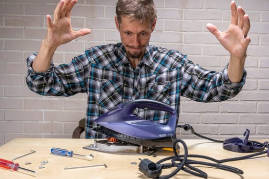 a funny and annoyed grief-stricken master repairs an electric iron. the master repairs the iron in the workshop on the table using tools. Disassembled electric iron.