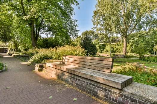 a bench in the middle of a park with trees and flowers on both sides, along an old brick path