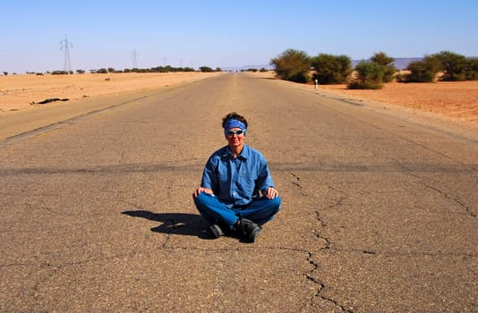 Young woman sitting cross-legged in the middle on the asphalt strip of a country road