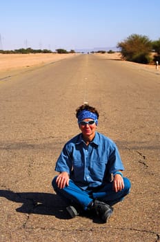 Young woman sitting cross-legged in the middle on the asphalt strip of a country road