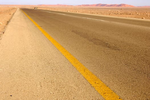 Tarred road with diagonal yellow boundary line at the edge of the Sahara near Al Aw
