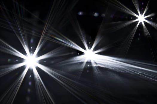 Bright headlights illuminating dark road at night with starburst effect.