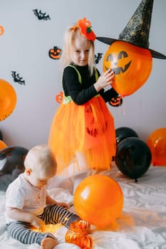 Children's Halloween - a girl in a witch hat and a carnival costume with airy orange and black balloons at home. Ready to celebrate Halloween.