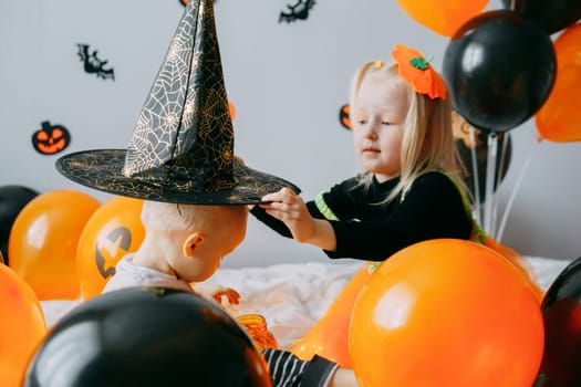 Children's Halloween - a girl in a witch hat and a carnival costume with airy orange and black balloons at home. Ready to celebrate Halloween.