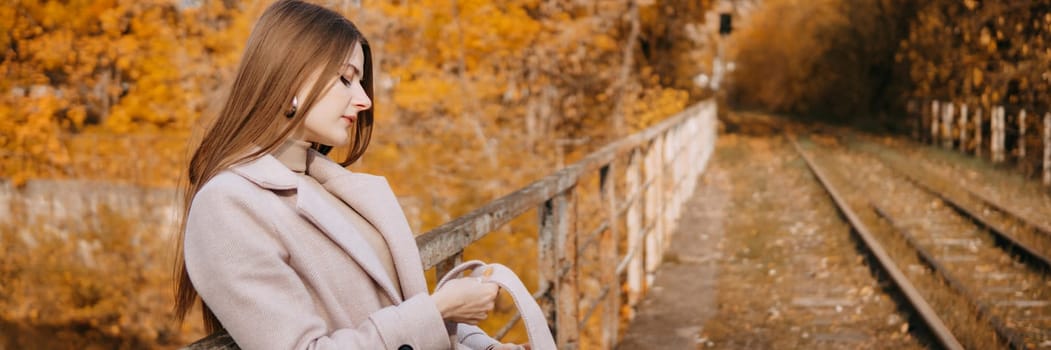 A beautiful long-haired woman walks through the autumn streets. Railway, autumn leaves, a woman in a light coat.