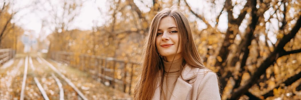 A beautiful long-haired woman walks through the autumn streets. Railway, autumn leaves, a woman in a light coat.