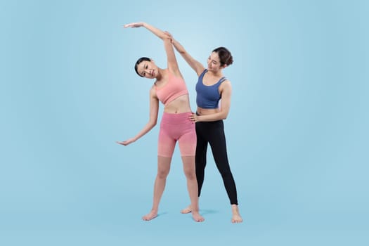 Asian woman in sportswear doing yoga exercise in standing pose with her trainer or yoga buddy. Healthy body care and meditation yoga lifestyle in full shot on isolated background. Vigorous