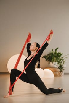 Girl in black doing fitness with red ribbons indoors.