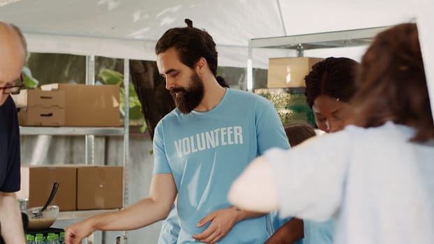 Elderly caucasian man on crutches is assisted by friendly black woman at a charitable food drive. Young volunteers giving humanitarian aid to the needy, homeless and handicapped people. Tripod shot.