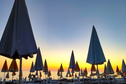 Closed beach umbrellas against background of sunset evening sky, concept of vacation and closing of season