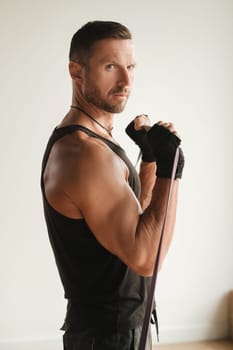 A man in black sportswear is engaged in strength fitness using a rubber loop indoors.