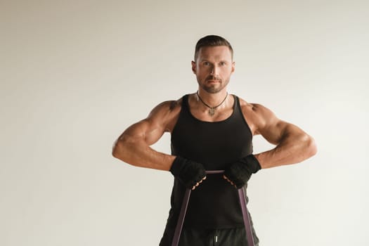 A man in black sportswear is engaged in strength fitness using a rubber loop indoors.