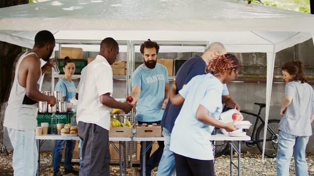 At humanitarian food drive, an elderly Caucasian guy with crutches is aided by a nice black woman. Young volunteers provide humanitarian relief to the poor, homeless, and disabled. Handheld shot.