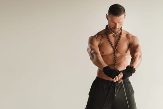 A man with a naked torso is engaged in strength fitness using a rubber loop indoors.