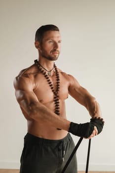 A man with a naked torso is engaged in strength fitness using a rubber loop indoors.