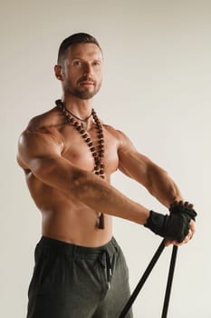 A man with a naked torso is engaged in strength fitness using a rubber loop indoors.