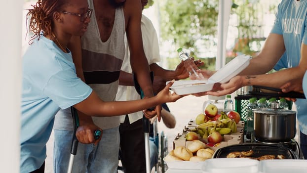 Voluntary individuals contributes to and offers humanitarian help to the underprivileged and needy. Young black volunteer woman helps african american guy using crutches at a food drive. Tripod shot.