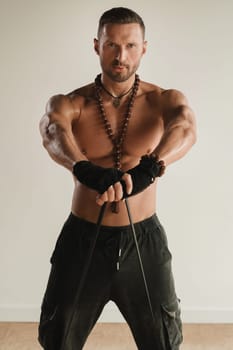 A man with a naked torso is engaged in strength fitness using a rubber loop indoors.