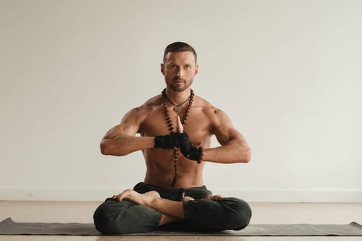 a man with a naked torso is sitting in the lotus position before doing yoga indoors. Fitness Trainer.