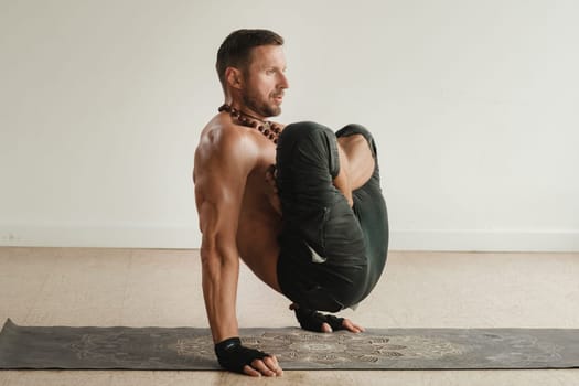 a man with a naked torso does yoga standing on his hands indoors. Fitness Trainer.