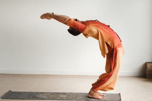 a man in an orange suit does yoga in a fitness room. The concept of health.