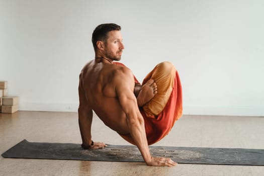 a man with a naked torso does yoga standing on his hands indoors. Fitness Trainer.