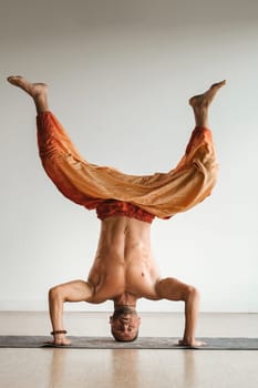 a man with a naked torso does yoga standing on his head indoors. Fitness Trainer.