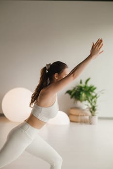 A girl in white clothes does yoga on a mat indoors.