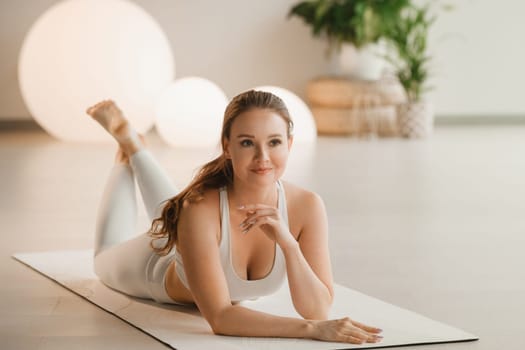 Portrait of a girl in white clothes lying on a mat before doing yoga indoors.