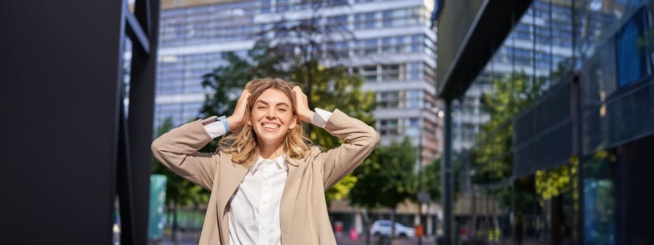 Excited businesswoman, office lady in suit, rejoicing, standing on street and celebrating, feeling happy, posing outdoors near office buildings.