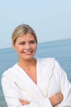 Smiling beautiful woman standing by the sea in bathrobe