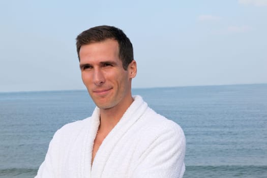 Smiling man standing by the sea in bathrobe