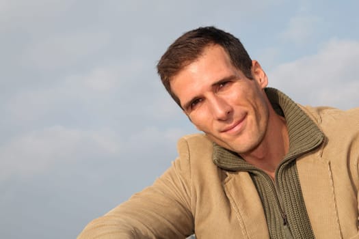 Smiling man sitting by the beach in autumn