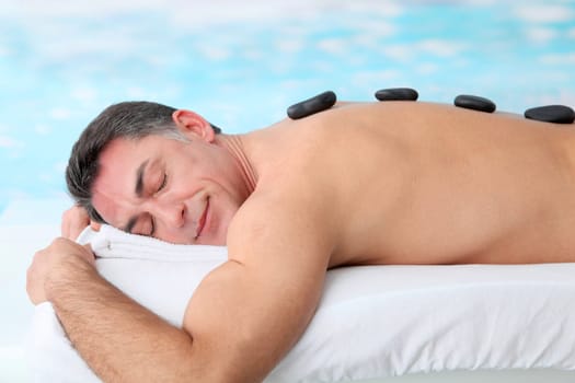 Man laying on massage bed with hot stones
