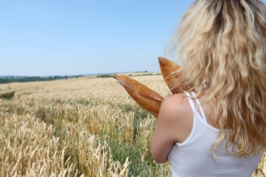 Blonde woman holding french bread in wheat field