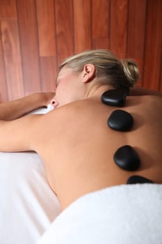 Blond woman laying on massage bed with hot stones