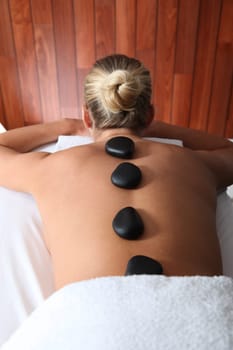Blond woman laying on massage bed with hot stones