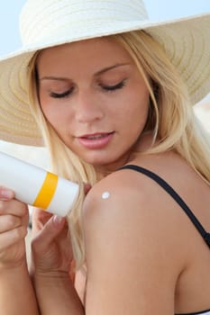 Blond woman putting sunscreen on her shoulder