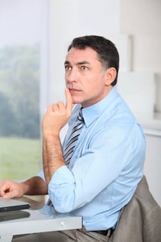 Businessman sitting at his desk with hand on chin
