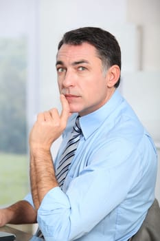 Businessman sitting at his desk with hand on chin