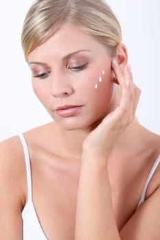 Beautiful blond woman putting facial moisturizer on her face