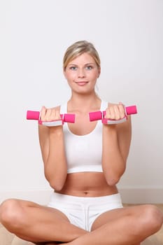 Beautiful blond woman lifting dumbbells in fitness gym