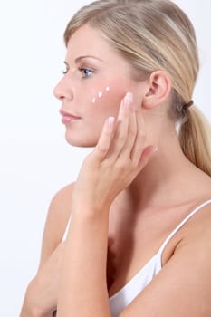Beautiful blond woman putting facial moisturizer on her face