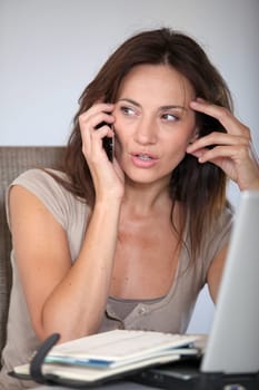 Woman working at home on laptop computer with telephone